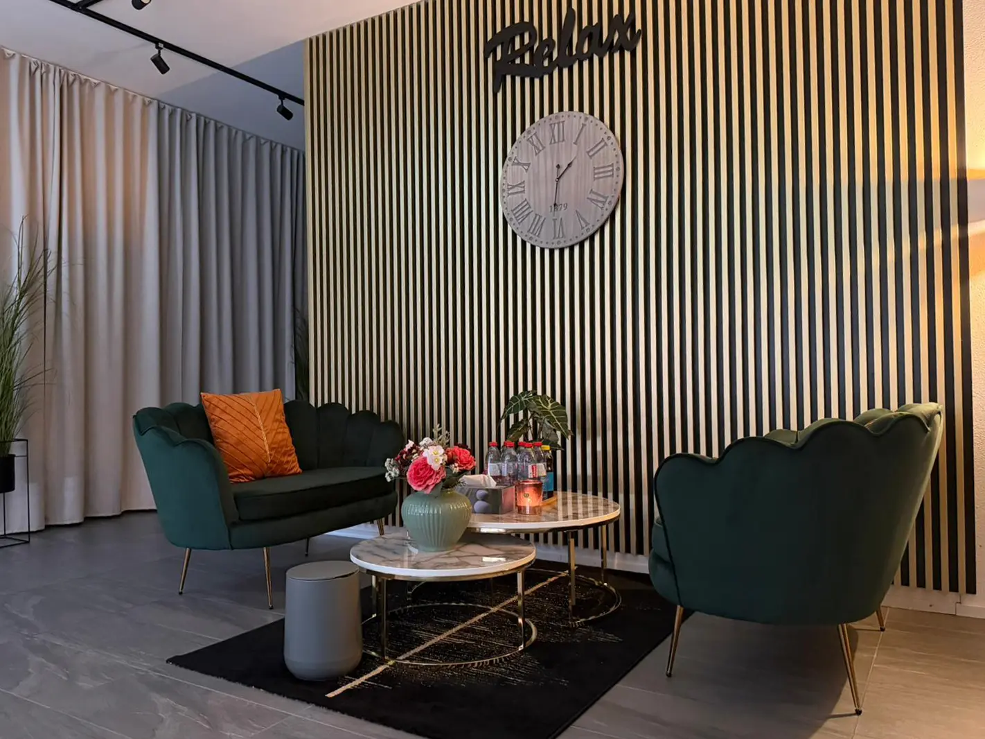 Modern waiting area with green chairs, striped wall, clock, and coffee tables
