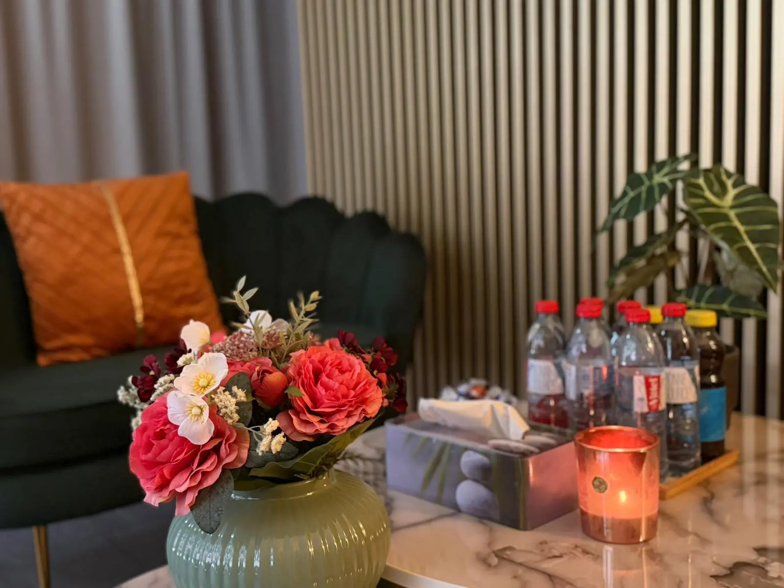 Cozy massage lounge with flowers, candle, drinks, and dark green seating