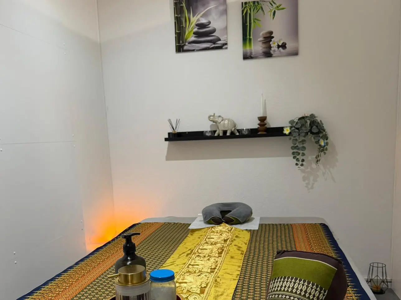 Thai massage room with a low mat, wall art, shelf decor, and warm lamp glow