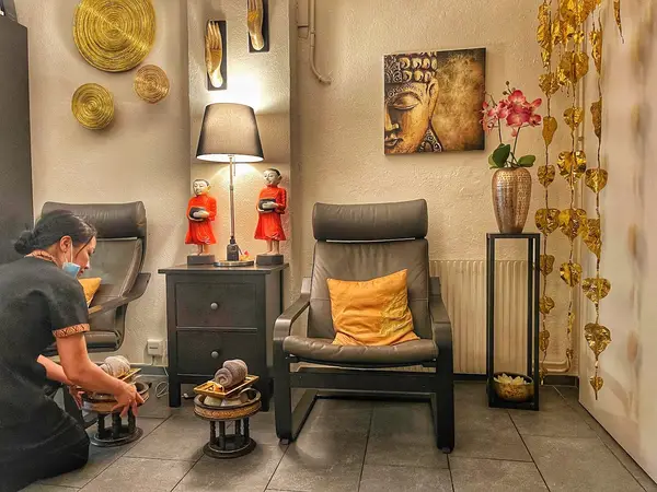 Cozy Thai spa waiting room with chairs, lamp, Buddha art, and gold decor