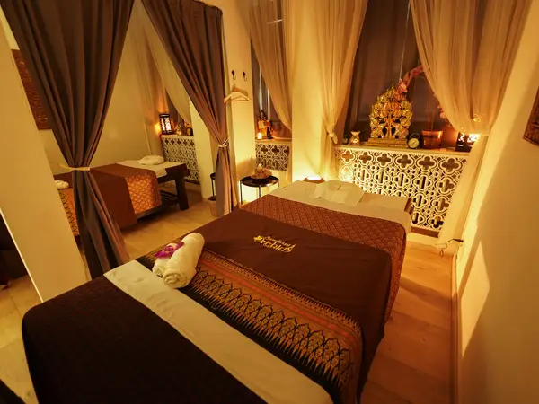 Warm Thai massage room with two curtained treatment beds and ornate decor
