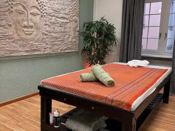 Thai massage treatment room with orange bedspread, towels, wall art, and potted plant