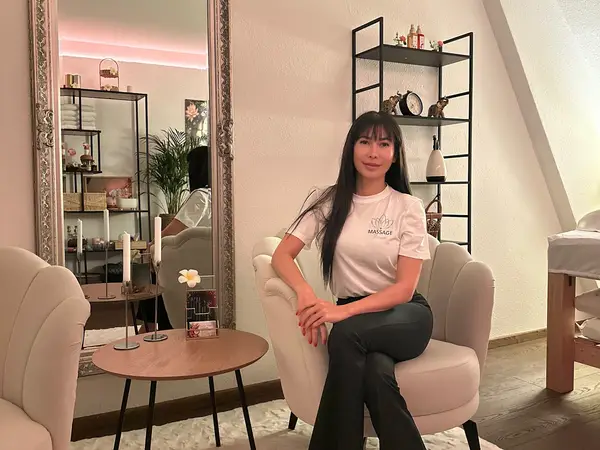 Cozy massage room with a seated woman, mirror, shelves, and soft lighting