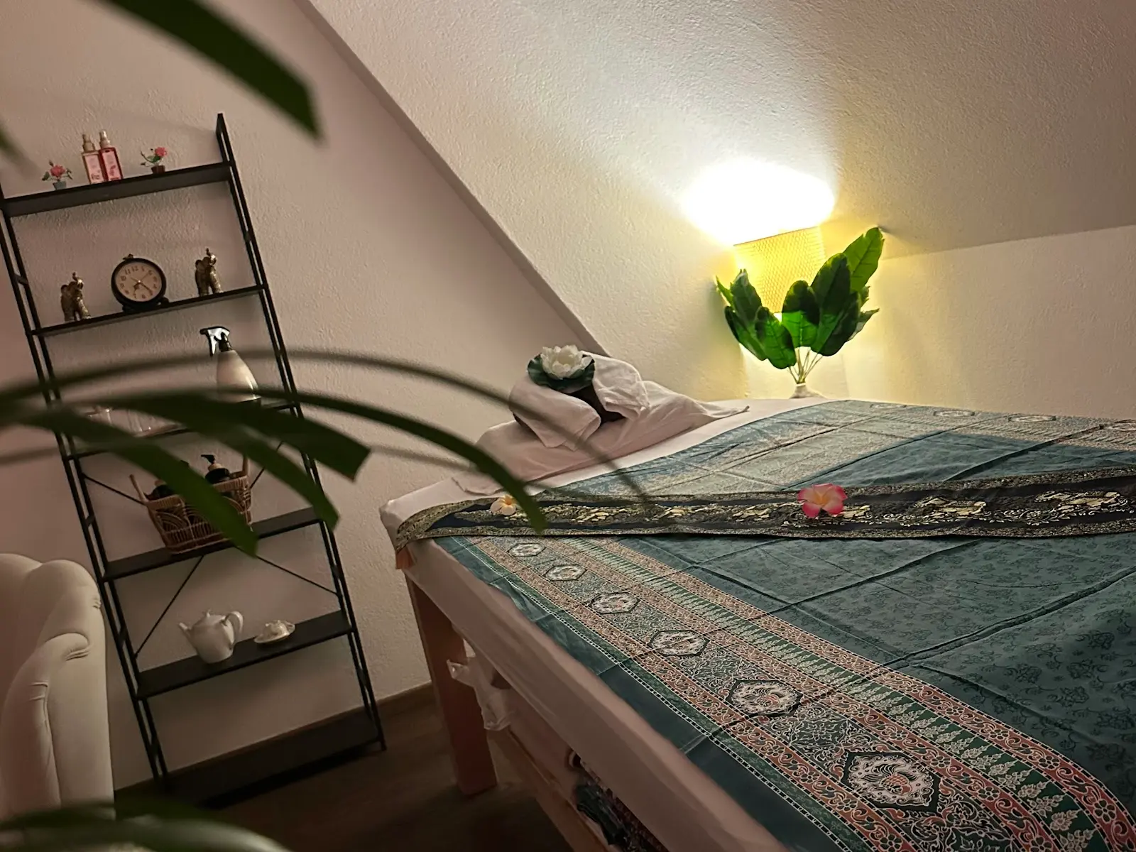 Cozy Thai massage room with a treatment table, shelf, lamp, and plants