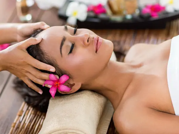 Woman receiving a head massage with pink flower decor in a spa setting