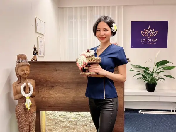 Wellness salon reception with Thai decor, plant, and staff member holding a garlanded tray