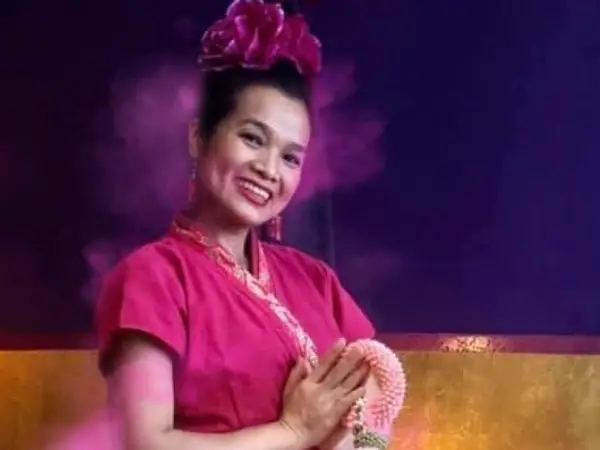 Smiling woman in pink Thai dress against a purple and gold backdrop