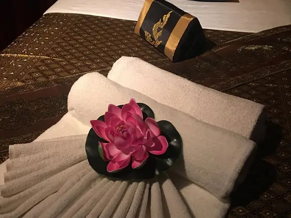 Massage table with folded towels, pink flower, and dark Thai-style decor