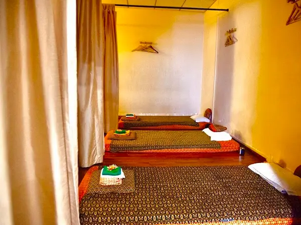 Warm Thai massage room with mats, curtains, pillows, and soft yellow lighting