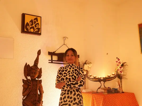 Warmly lit massage room with Thai decor, candles, and a standing woman