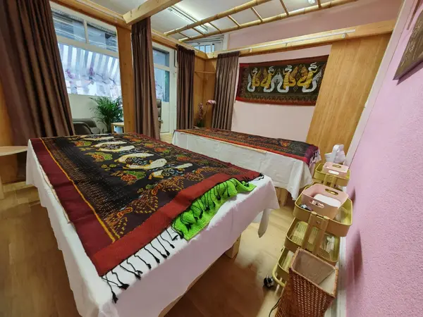Thai massage room with two covered tables, curtains, wooden decor, and warm lighting