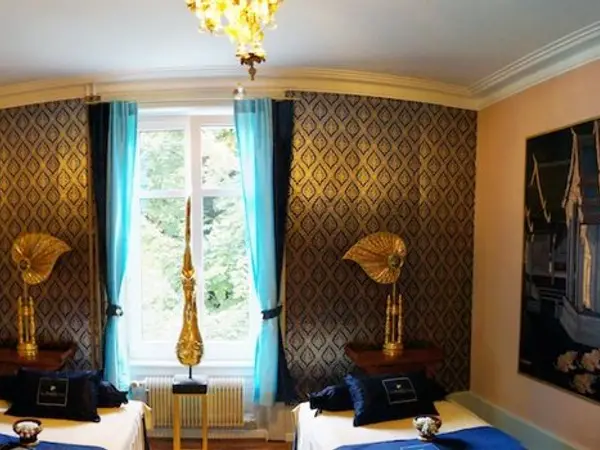 Elegant massage room with twin beds, ornate wallpaper, blue curtains, and gold decor
