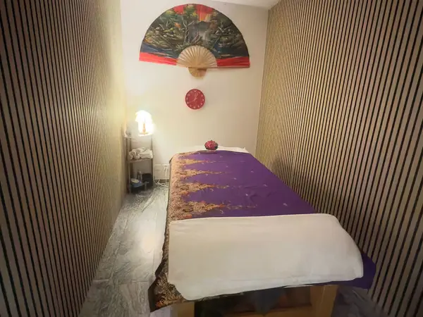 Small massage room with striped walls, purple treatment bed, and decorative fan