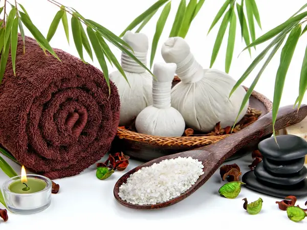 Spa still life with rolled towels, herbal compresses, candle, rice, and stacked stones