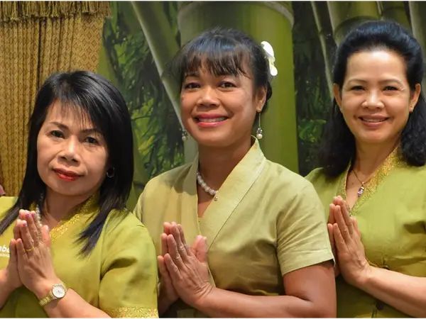 Three smiling women in green uniforms with palms pressed together