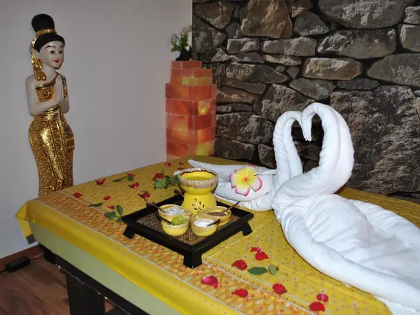 Thai massage room with decorative statue, stone wall, and towel swans on a bed