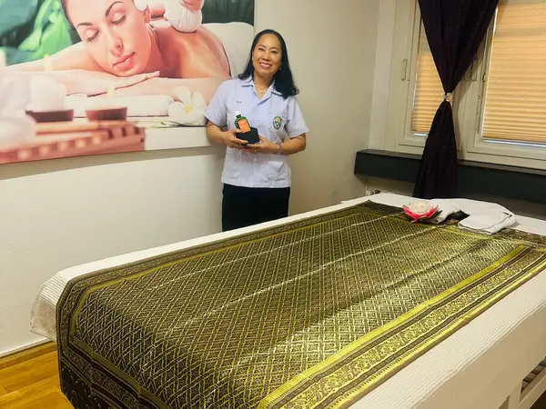 Thai massage treatment room with bed, wall art, and smiling therapist