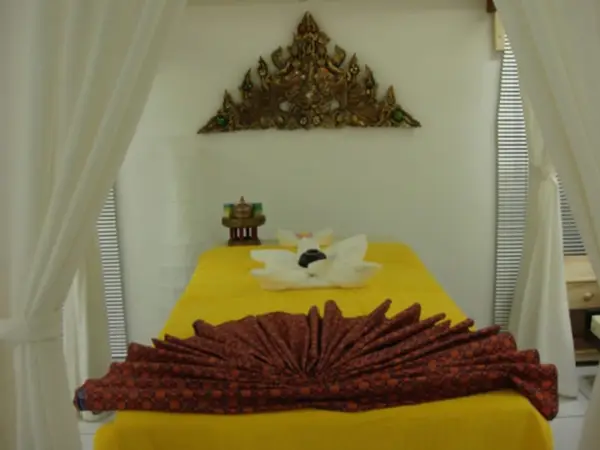Thai massage treatment bed with yellow cover, white curtains, and ornate wall decor