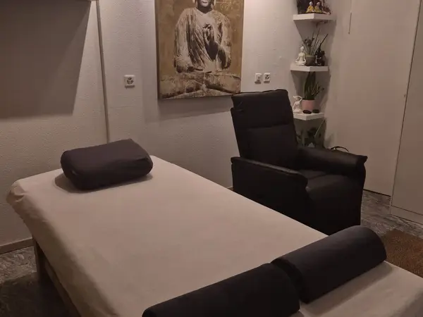 Massage room with treatment bed, black chair, wall art, and shelves