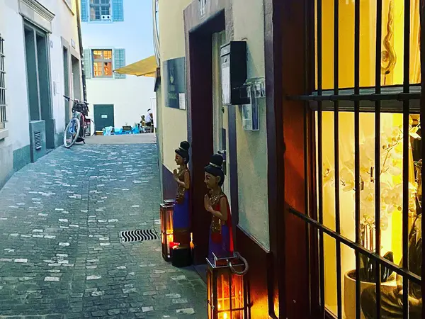 Narrow cobblestone alley with a warmly lit Thai massage entrance and decorative statues