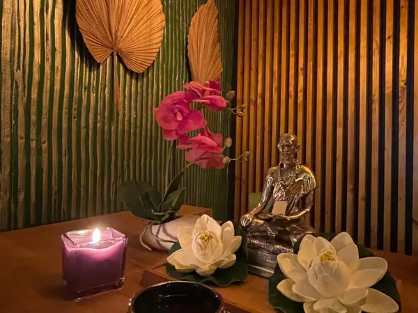 Candlelit spa corner with Buddha statue, flowers, and bamboo wall decor