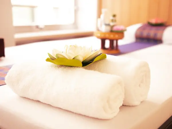 Massage table with rolled white towels and a flower in a bright spa room
