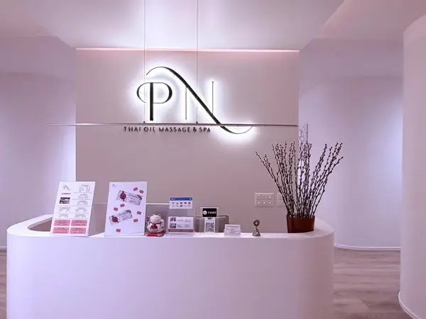 Minimalist spa reception with glowing PN sign, curved desk, and dried branches