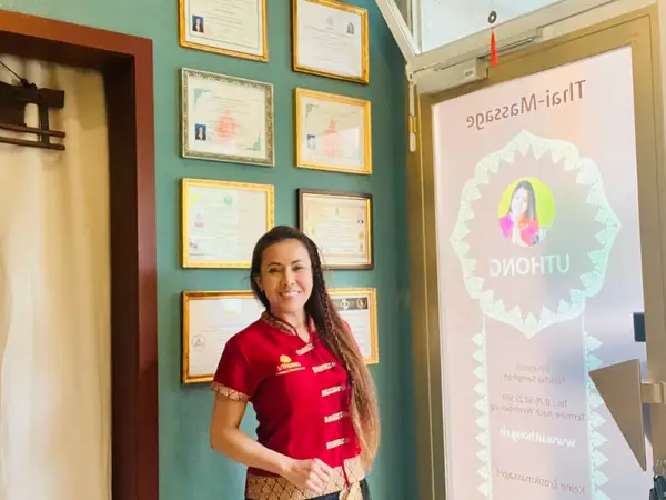 Woman in red stands in a certificate-lined Thai massage salon lobby