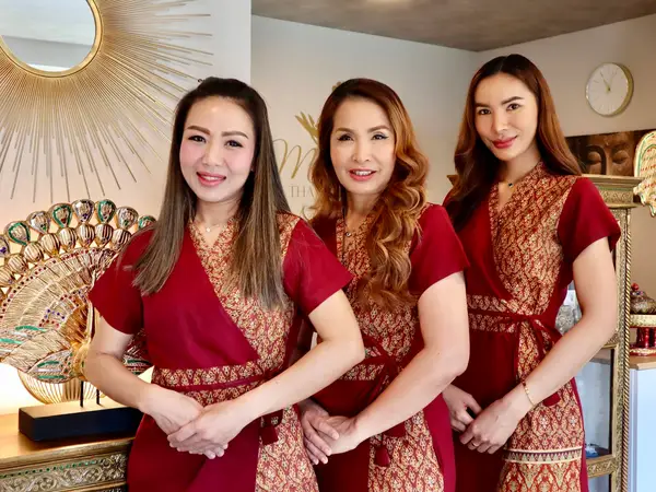 Three women in red Thai uniforms stand in a decorated salon interior