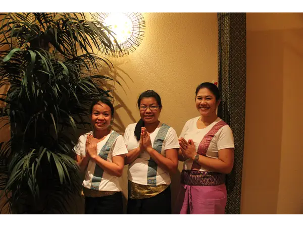 Three smiling staff members pose indoors beside a large potted plant