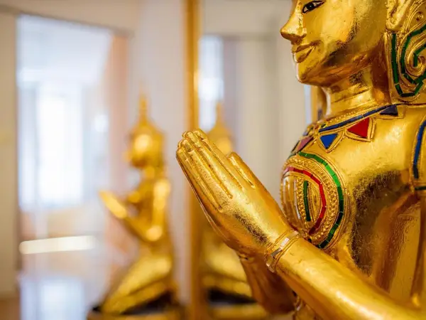 Golden Thai statues with prayer hands in a softly lit interior