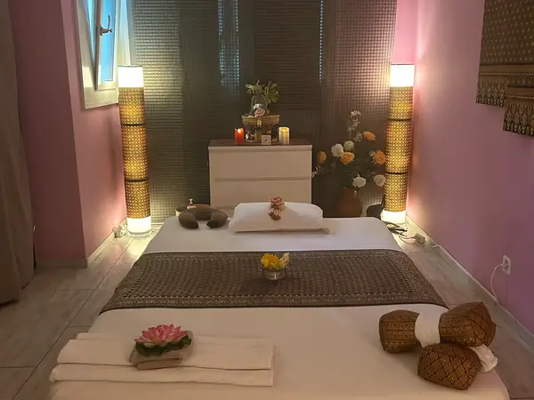 Cozy Thai massage room with two floor mats, pink walls, and warm lamps