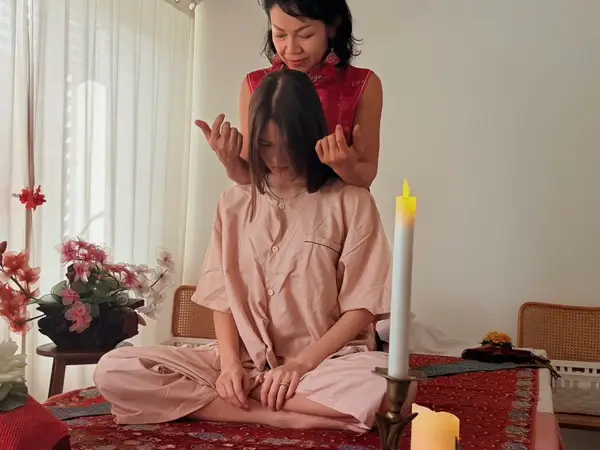 Thai massage room with two women, candles, flowers, and a woven chair