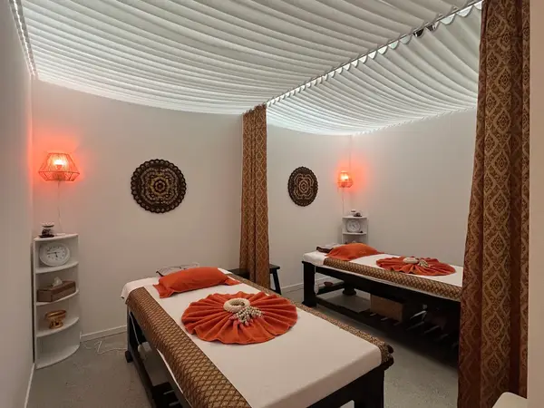 Serene massage room with two treatment beds, warm lamps, and Thai-style decor