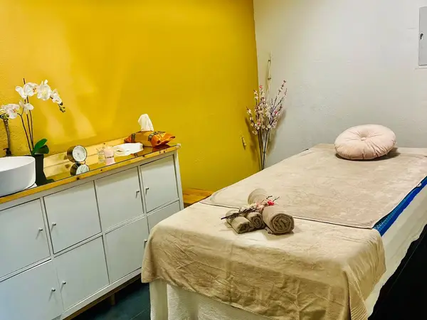 Massage room with beige treatment bed, white cabinet, and yellow accent wall