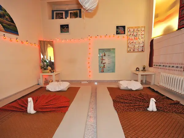 Warm Thai massage room with two floor mats, cushions, and string lights