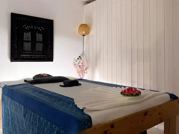 Serene massage room with wooden table, blue linens, flowers, and warm lighting