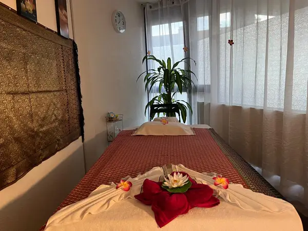 Massage room with two Thai-style tables, sheer curtains, and a potted plant