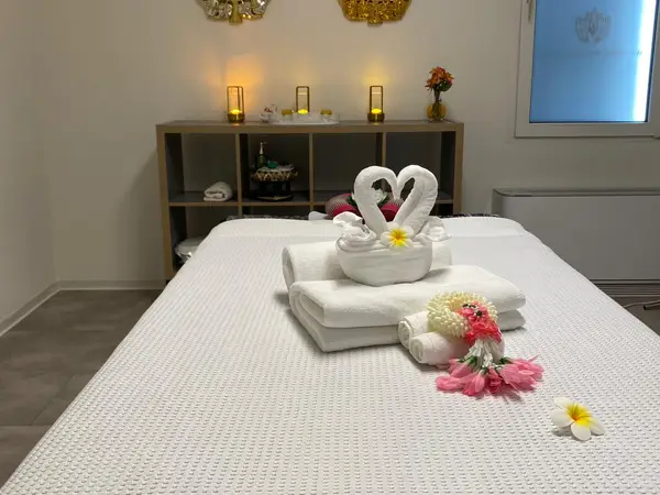Massage room with neatly made bed, folded towels, candles, and floral decor
