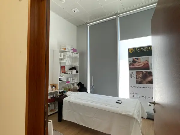 Bright massage room with treatment table, shelves, and closed gray blinds