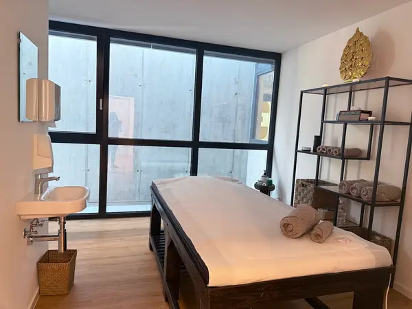 Minimal massage room with treatment table, sink, shelving, and large frosted windows