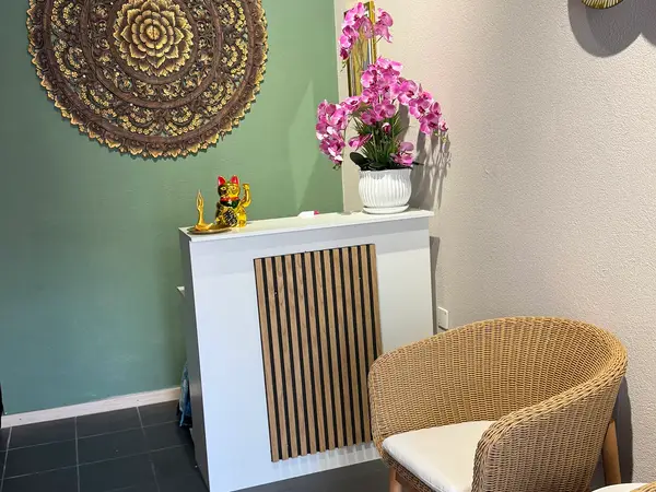Thai massage reception with wicker chair, orchid, and ornate wall decor