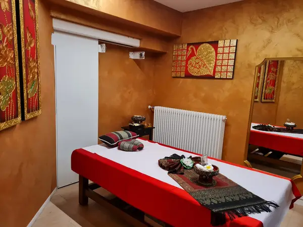 Thai-massage treatment room with red table, gold wall decor, and mirror