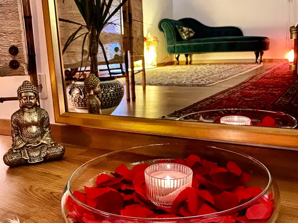 Cozy massage room with Buddha decor, candles, mirror, and green chaise lounge