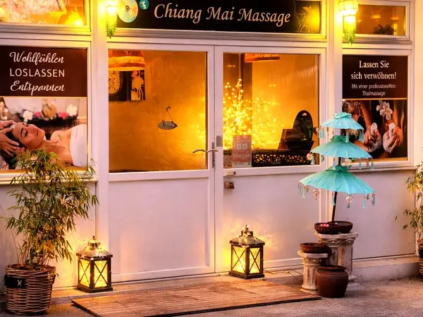 Warmly lit Thai massage storefront with signs, lanterns, and potted plants