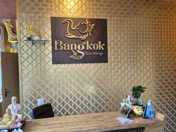 Thai massage reception with gold patterned wallpaper, sign, and wooden desk