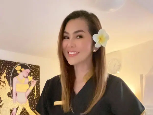 Smiling woman in black uniform inside softly lit Thai massage room