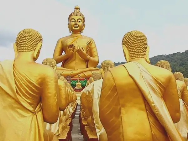 Outdoor temple scene with rows of golden Buddha statues facing a giant Buddha
