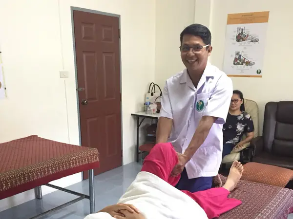 Thai massage room with therapist stretching a client, chairs and wall poster nearby