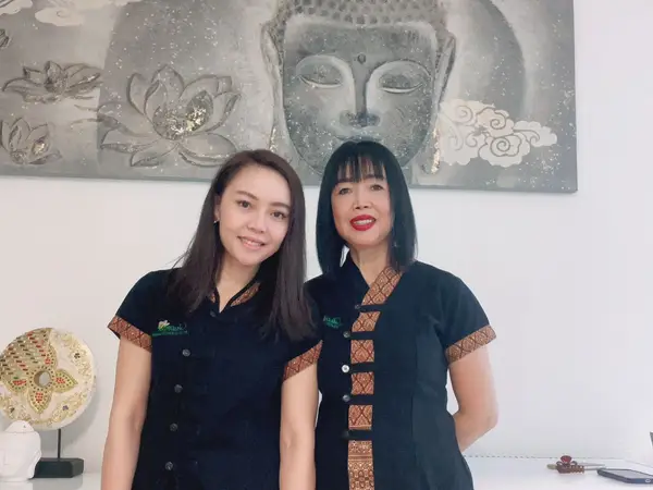 Two women in black uniforms stand before a Buddha wall artwork